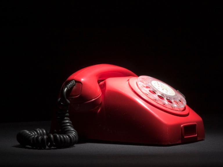 Roter Vintage-Telefon mit drehbarem Ziffernblatt auf schwarzem Hintergrund.